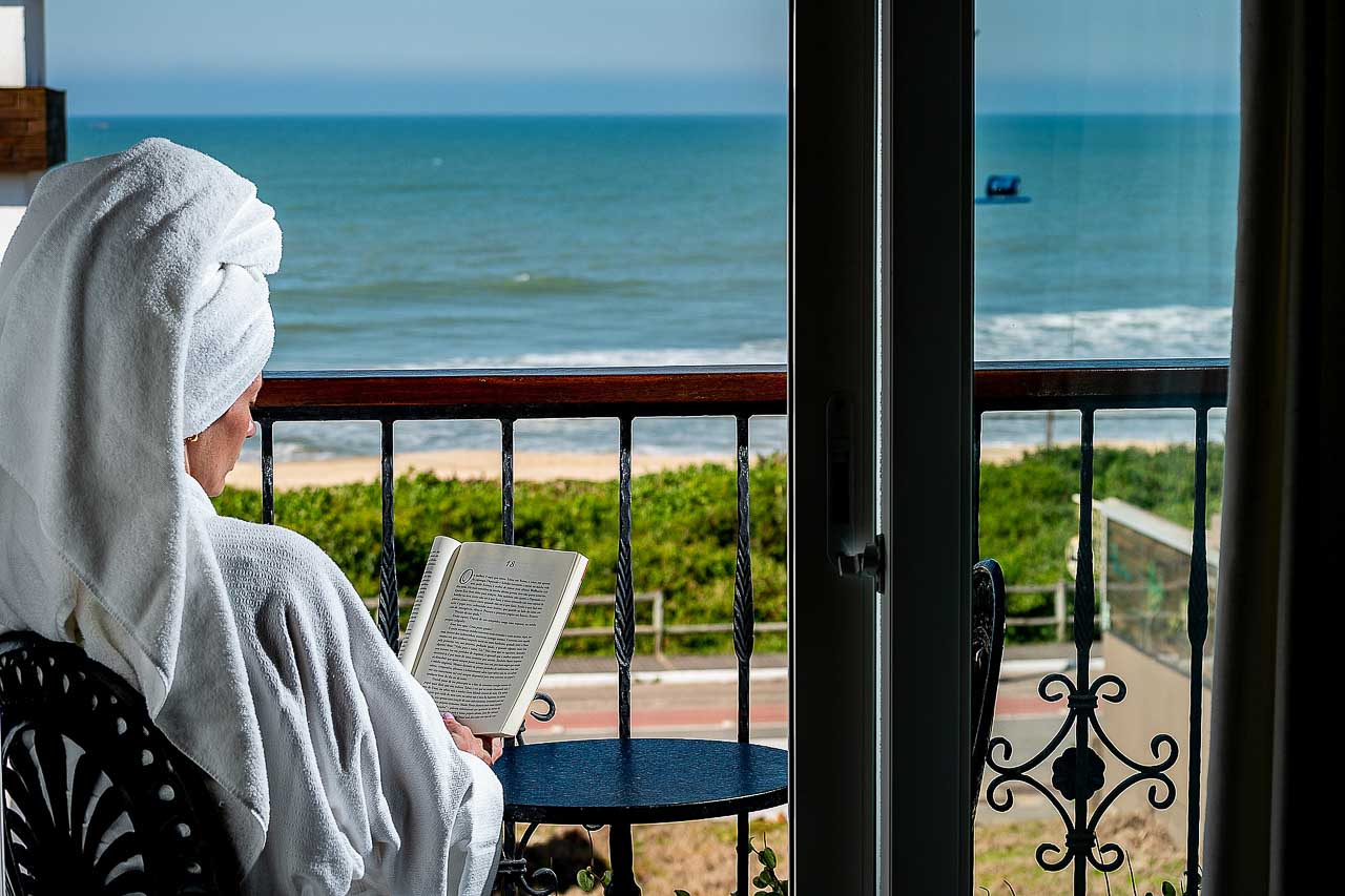 Hospede lendo um livro na sacada do hotel na Praia Brava, o quarto tem vista mar.