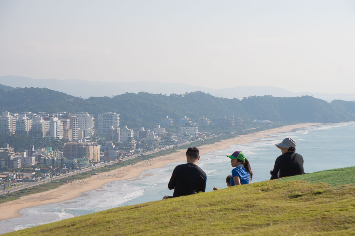 Família sentada no topo do Morro do Careca olhando a paisagem da Praia Brava, Itajaí. 